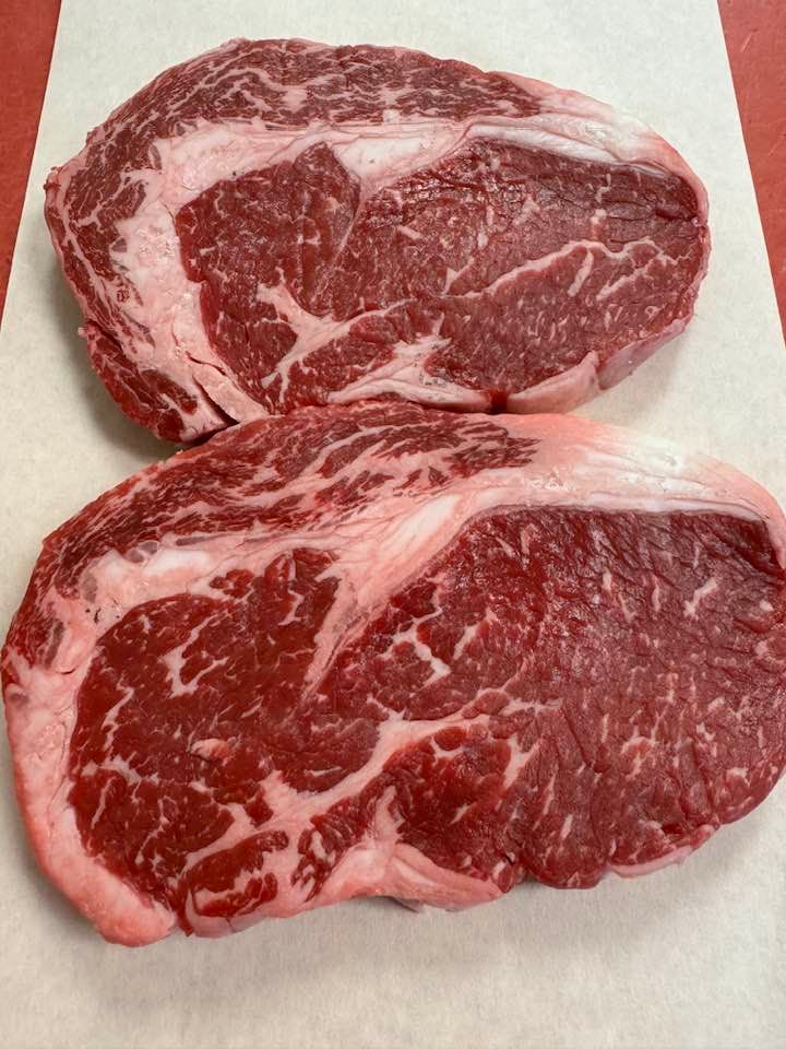 Two raw ribeye steaks on white butcher paper.