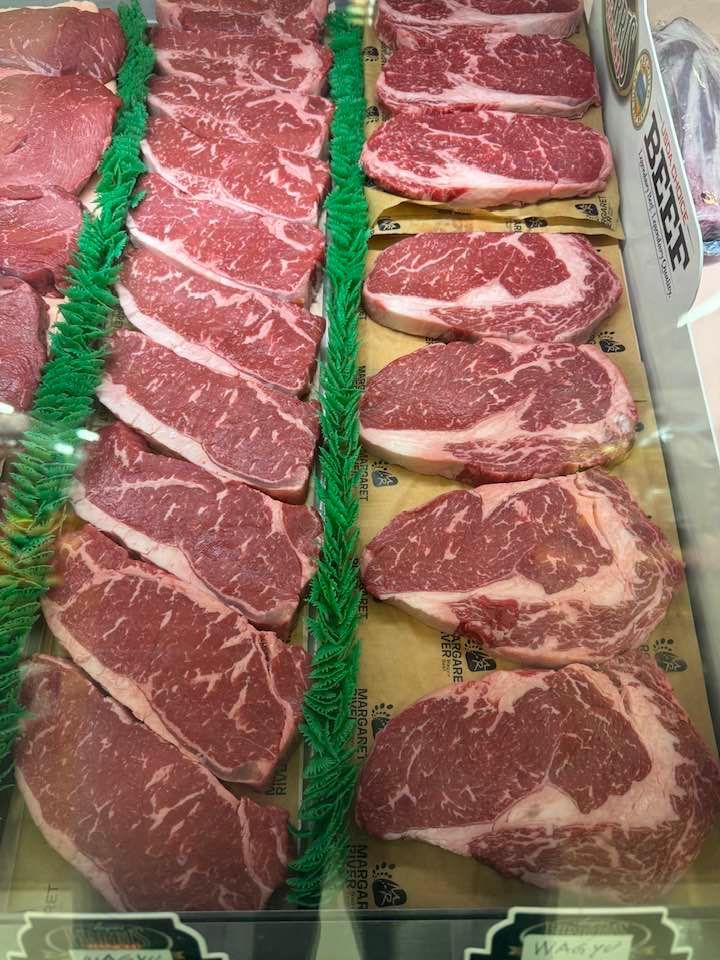 Display case of raw beef steaks: sirloins and ribeyes, red with marbling, in a grocery store.
