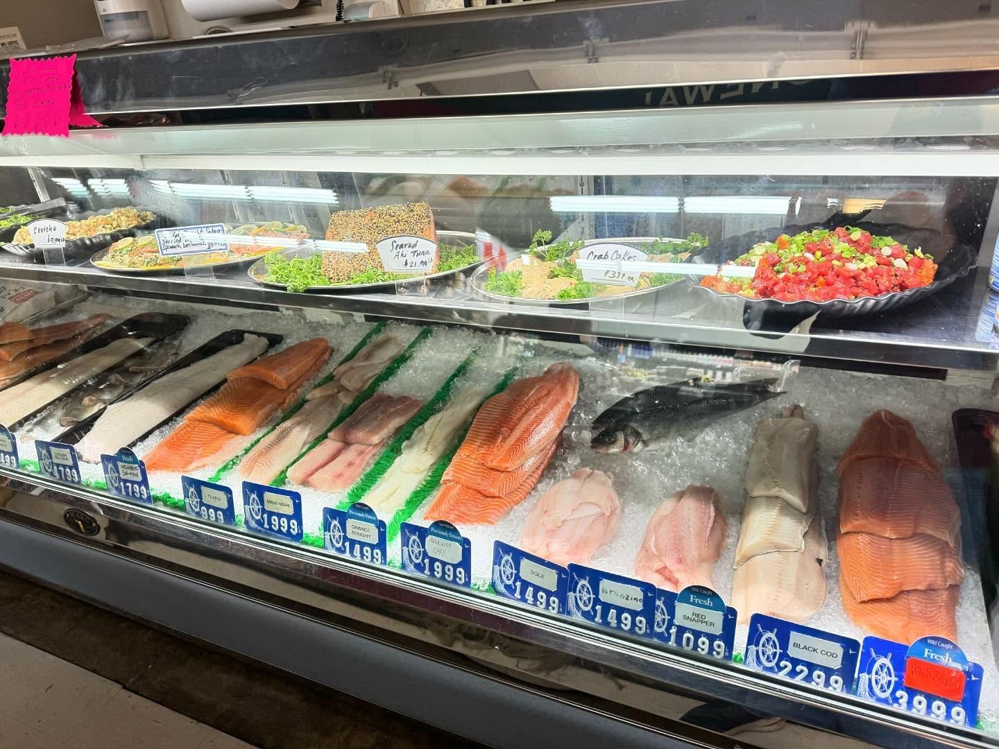 Seafood display case with various fish fillets and prepared dishes on ice.
