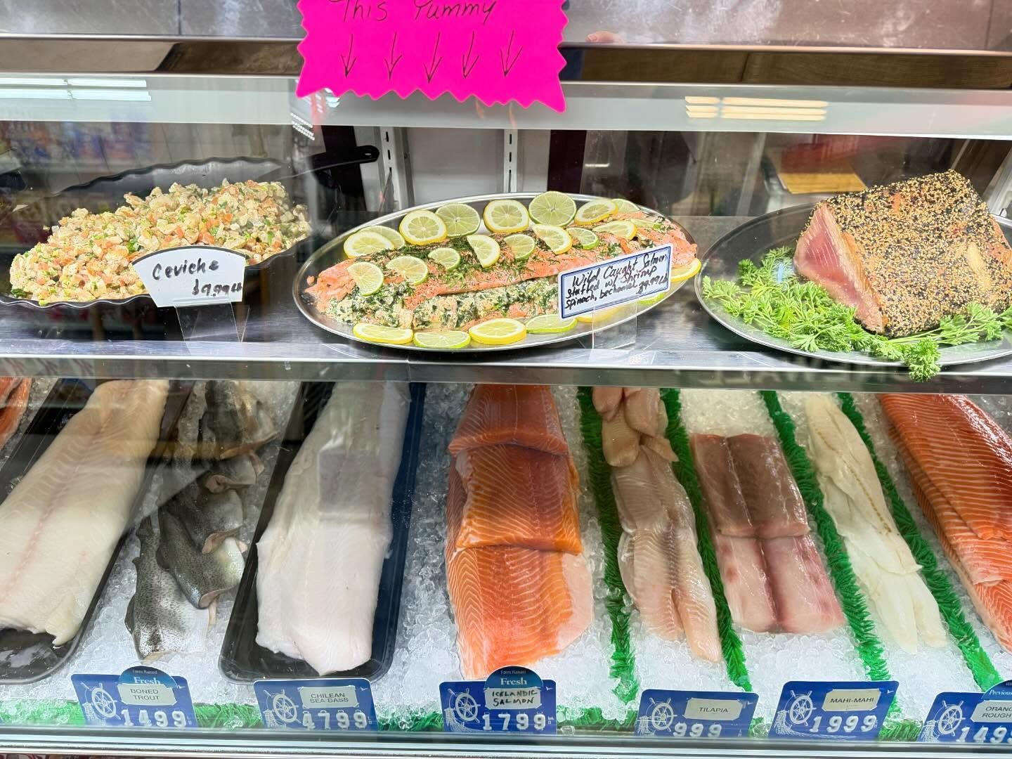 Seafood display case: various prepared fish and raw fillets on ice.