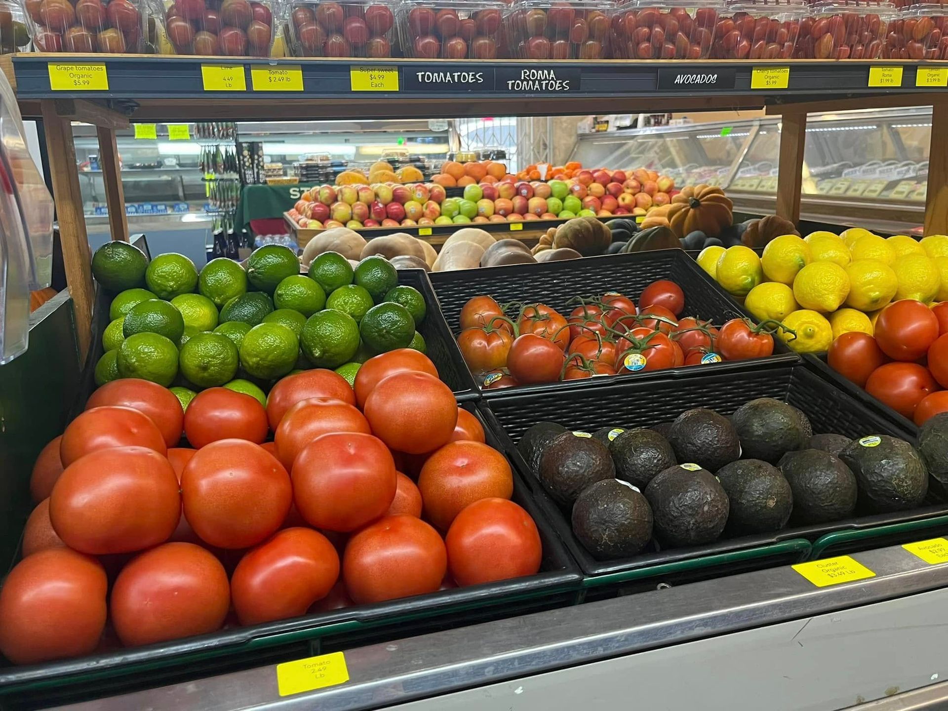 Produce section in a grocery store displaying tomatoes, limes, avocados, and lemons.