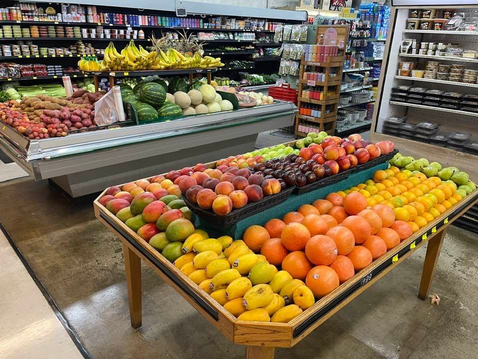 A grocery store fruit display with mangoes, oranges, peaches, and grapes.
