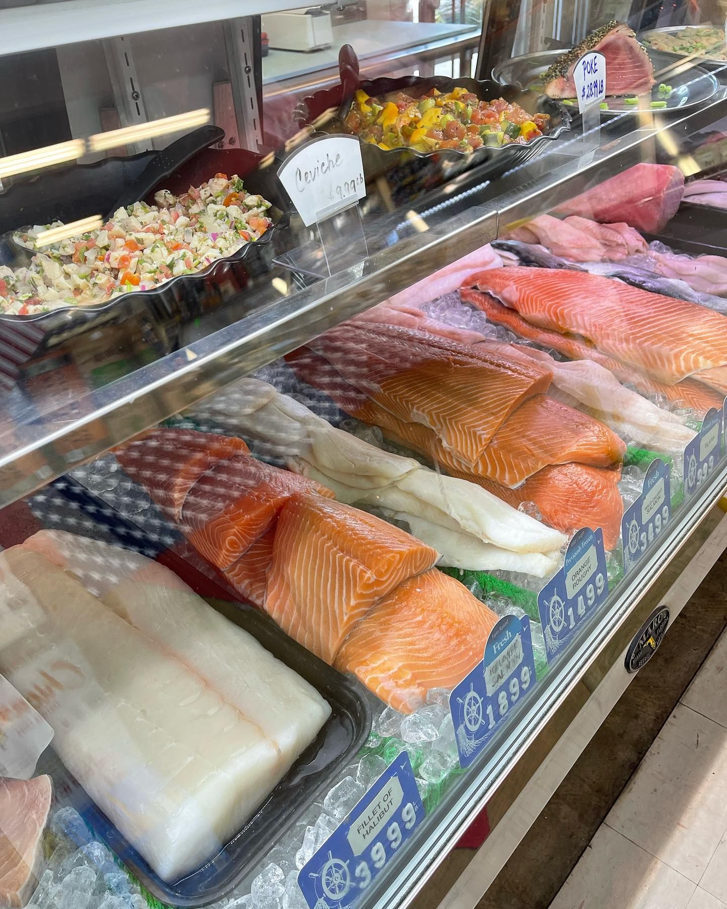 Seafood display case with various fish fillets on ice and prepared salads.