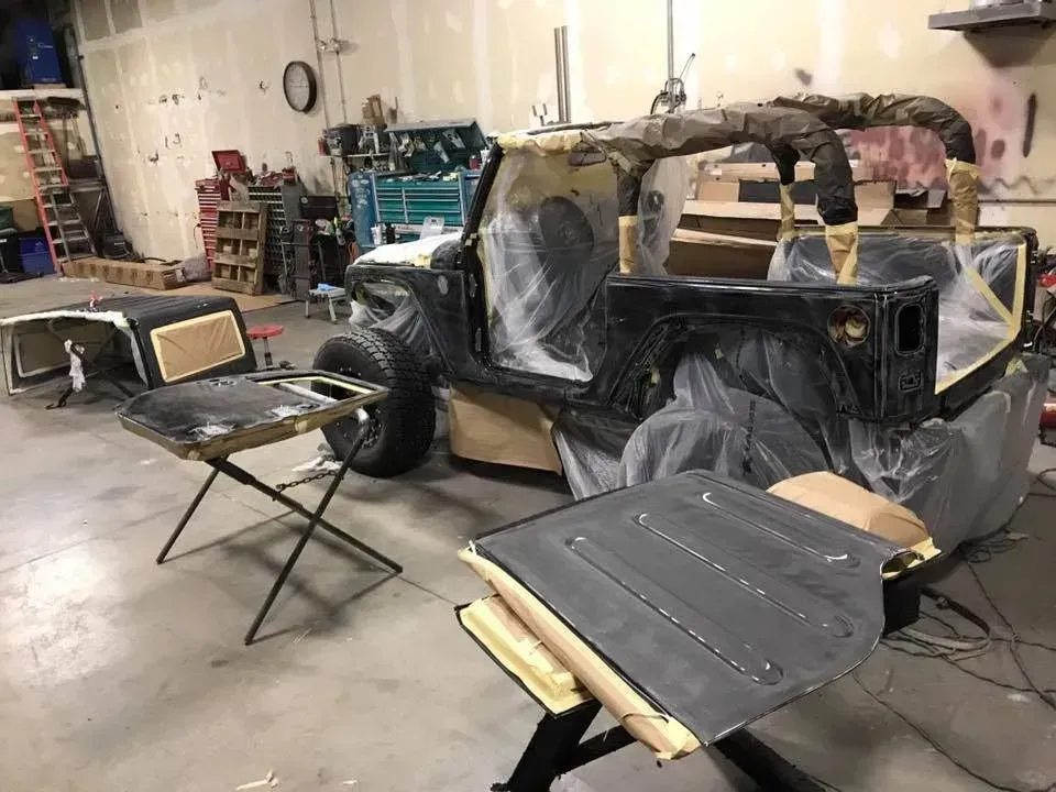 Jeep being painted in a workshop. Parts on stands, vehicle masked, ready for paint.