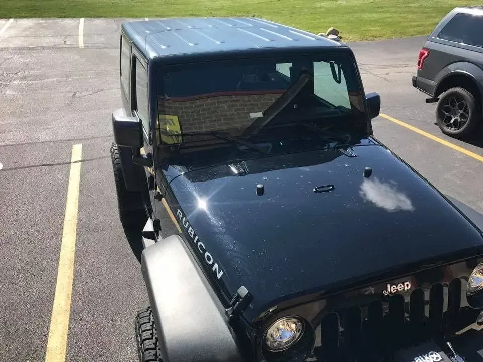 Black Jeep Rubicon parked on asphalt, sunny day.
