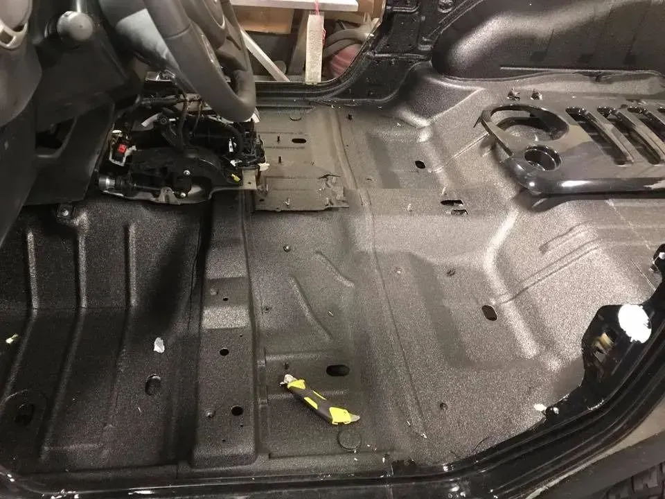Black interior of a vehicle floor, treated with textured coating; tools visible.