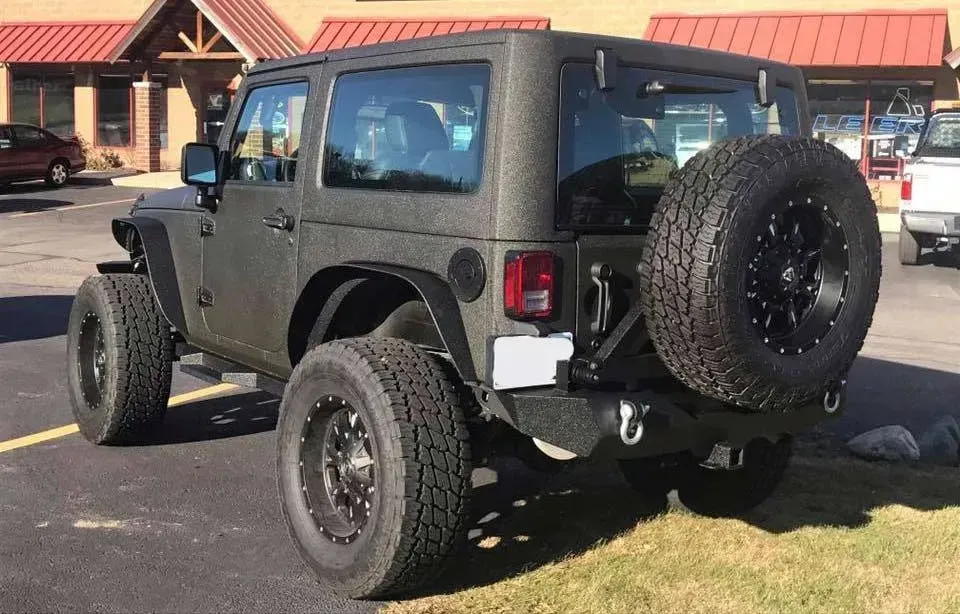 Dark green Jeep Wrangler with large tires and spare on the back, parked outdoors.