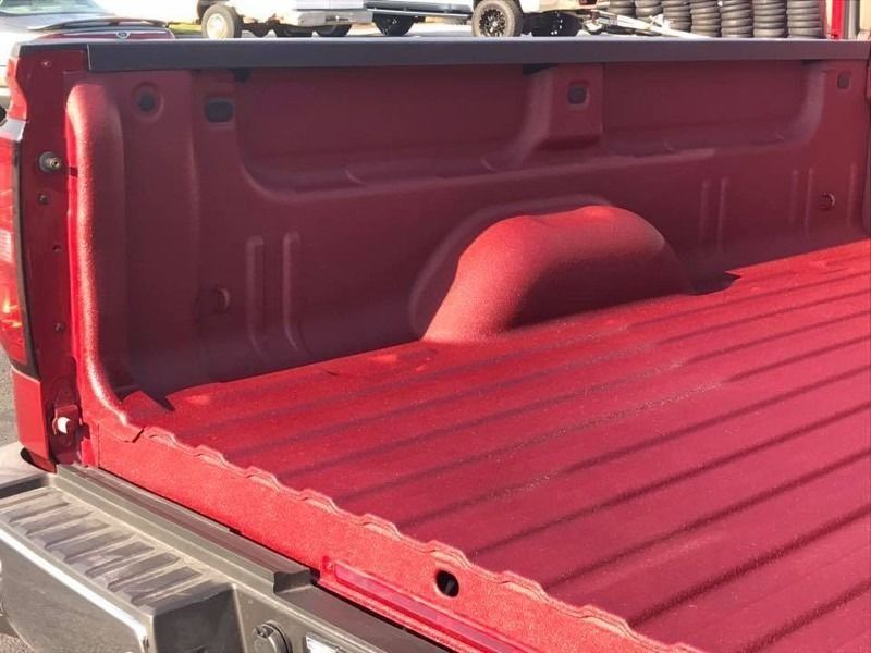 Red pickup truck bed with spray-in bedliner, showing ridges and wheel well.