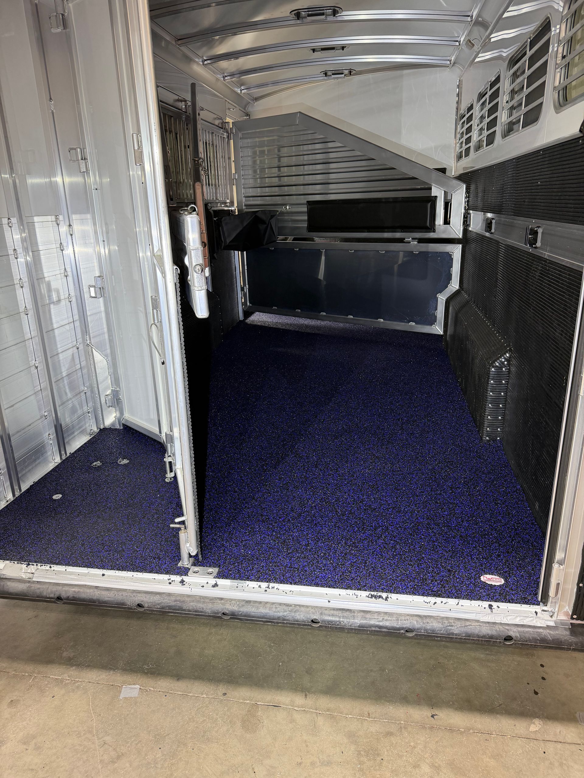 Empty white trailer interior with dark blue carpeted floor and metal shelving panels