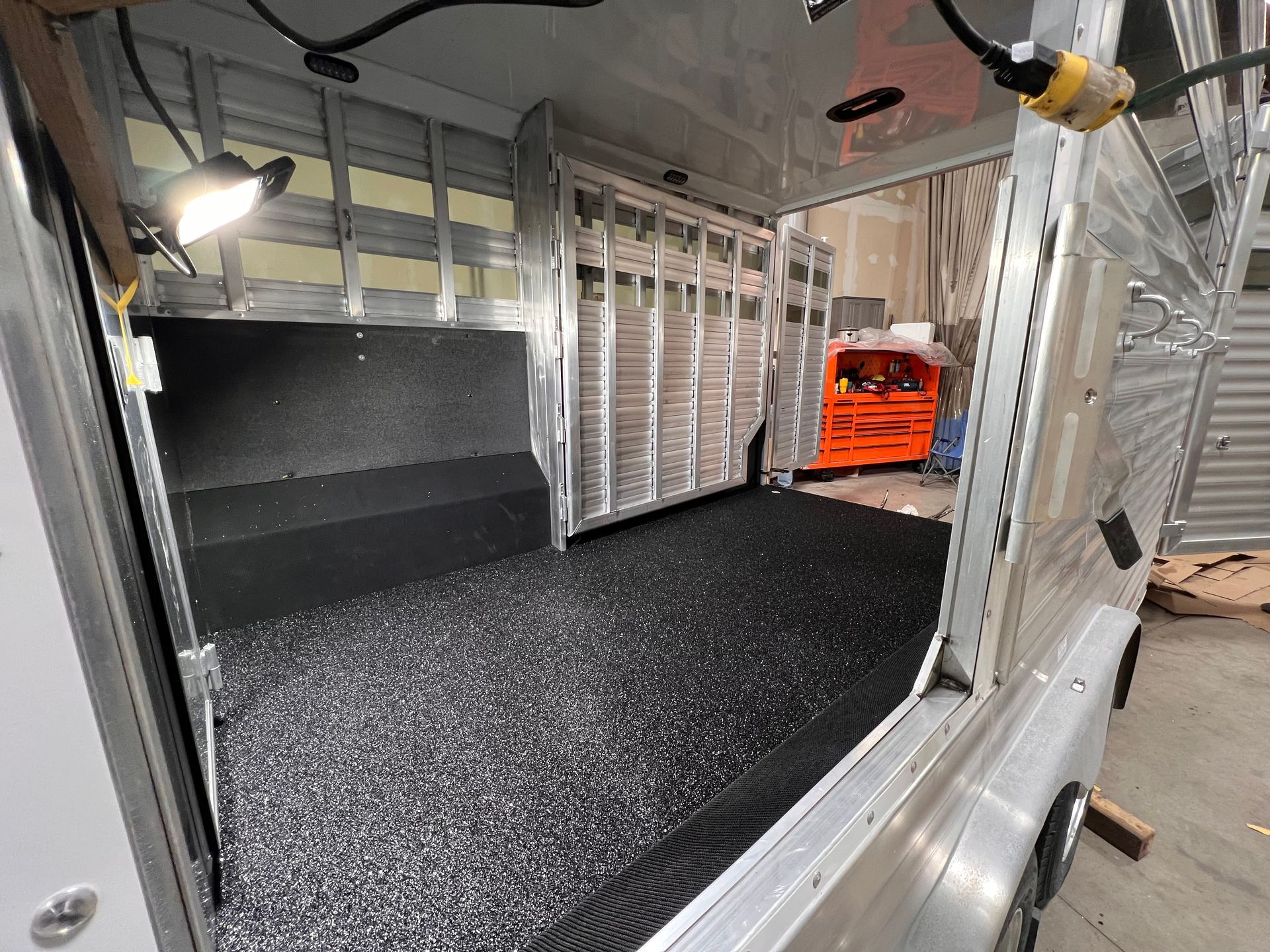 Empty cargo van interior with black flooring, silver walls, and orange tools at the back