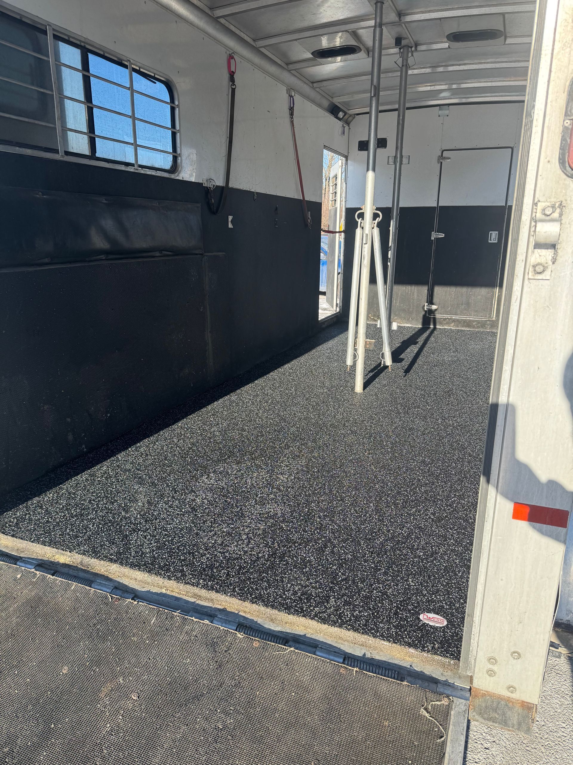 Inside a bus or trailer interior with black walls, a speckled floor, windows, and white support posts.