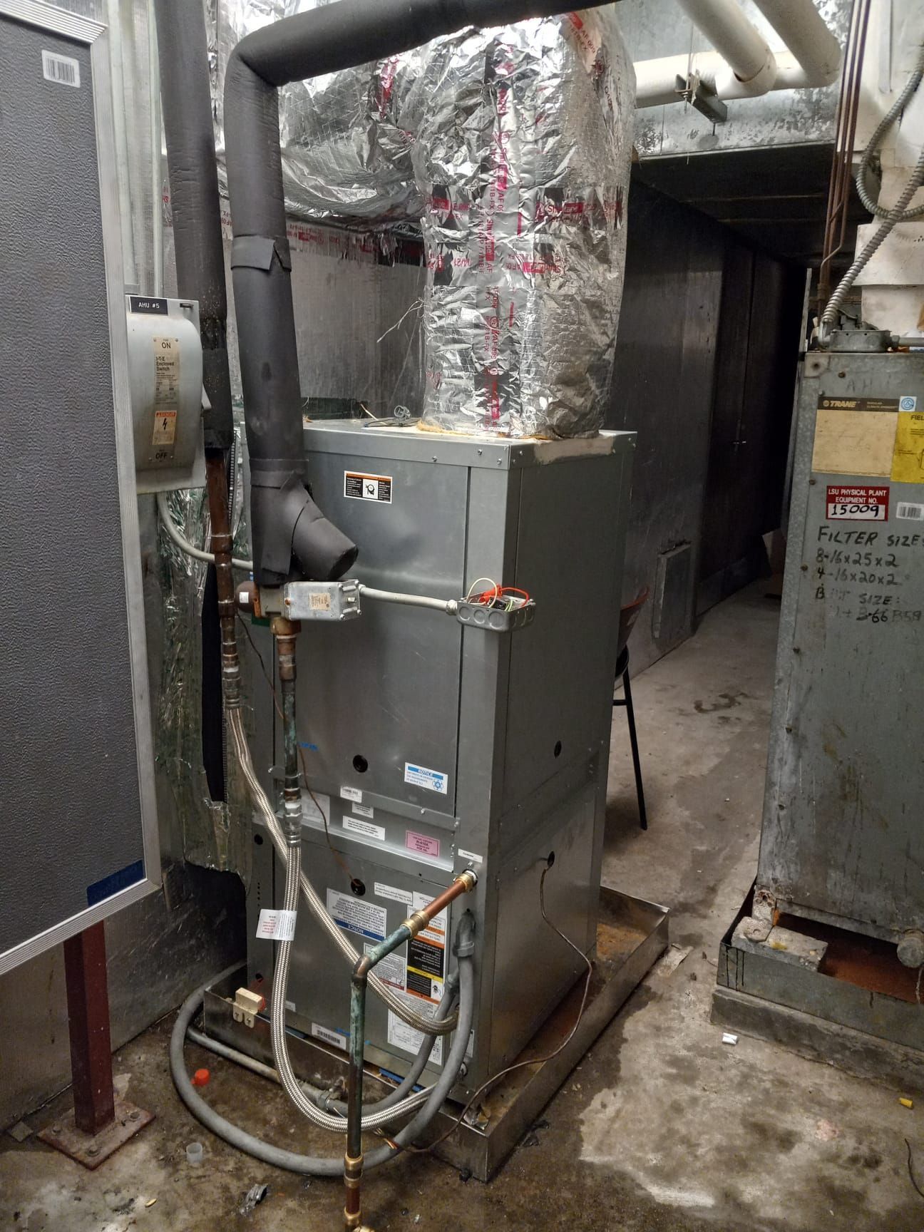 Industrial HVAC furnace with insulated ductwork and pipes in a utility room.