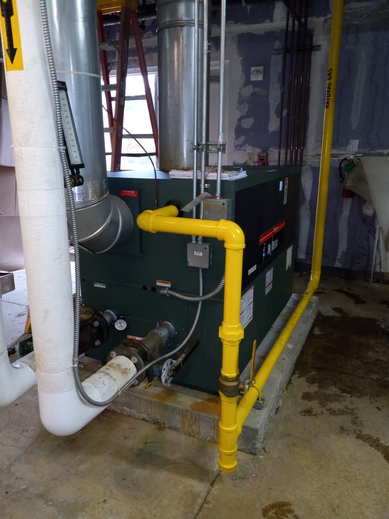 Yellow gas pipe beside a green HVAC unit in a basement utility room