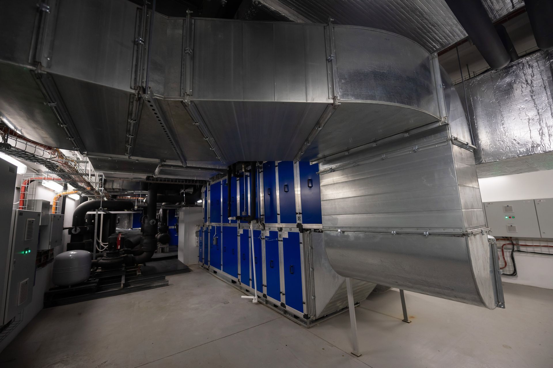 Industrial mechanical room with shiny silver ductwork and blue equipment cabinets