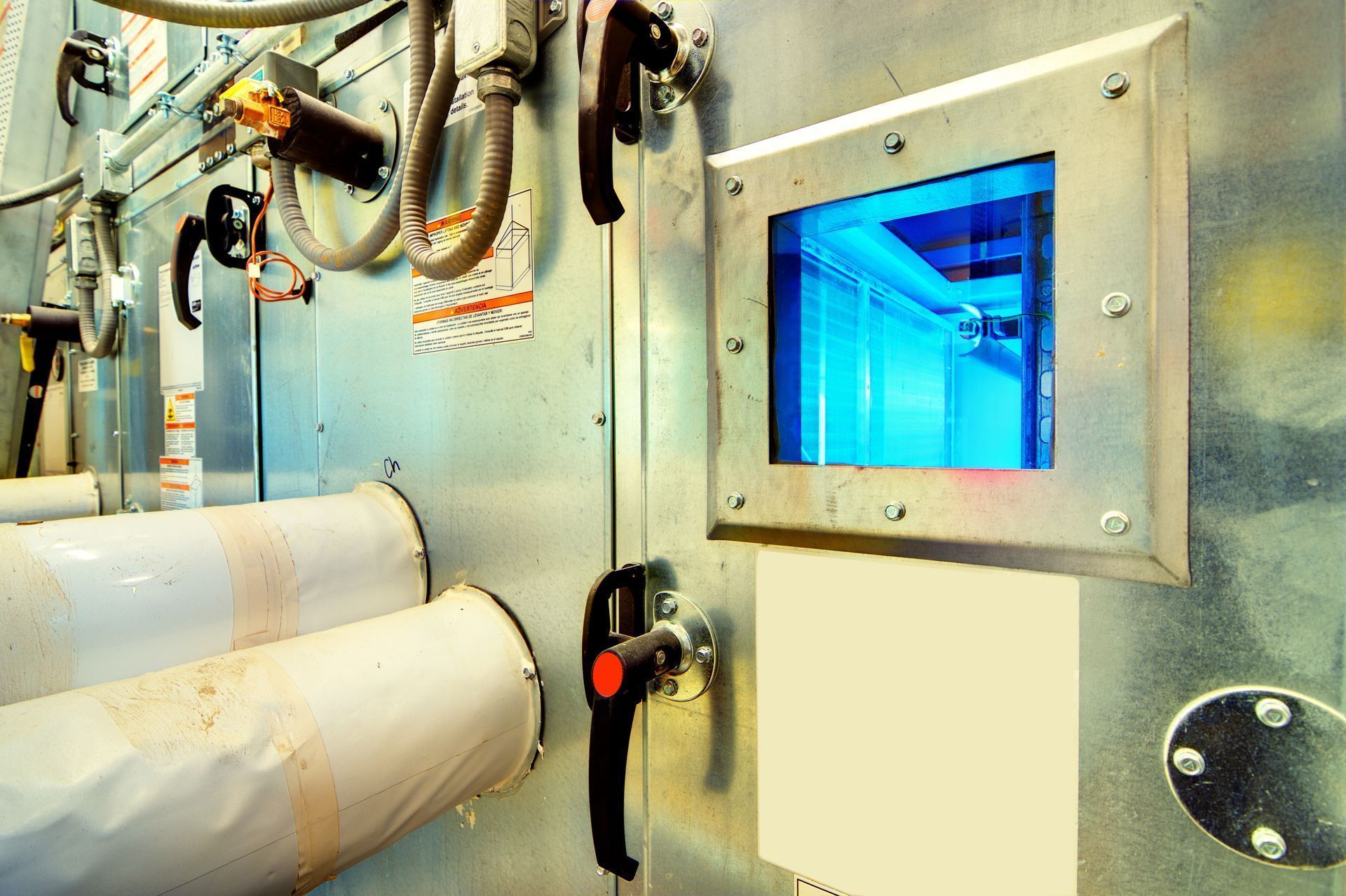 Industrial machinery with pipes and a blue-lit inspection window on a metal panel