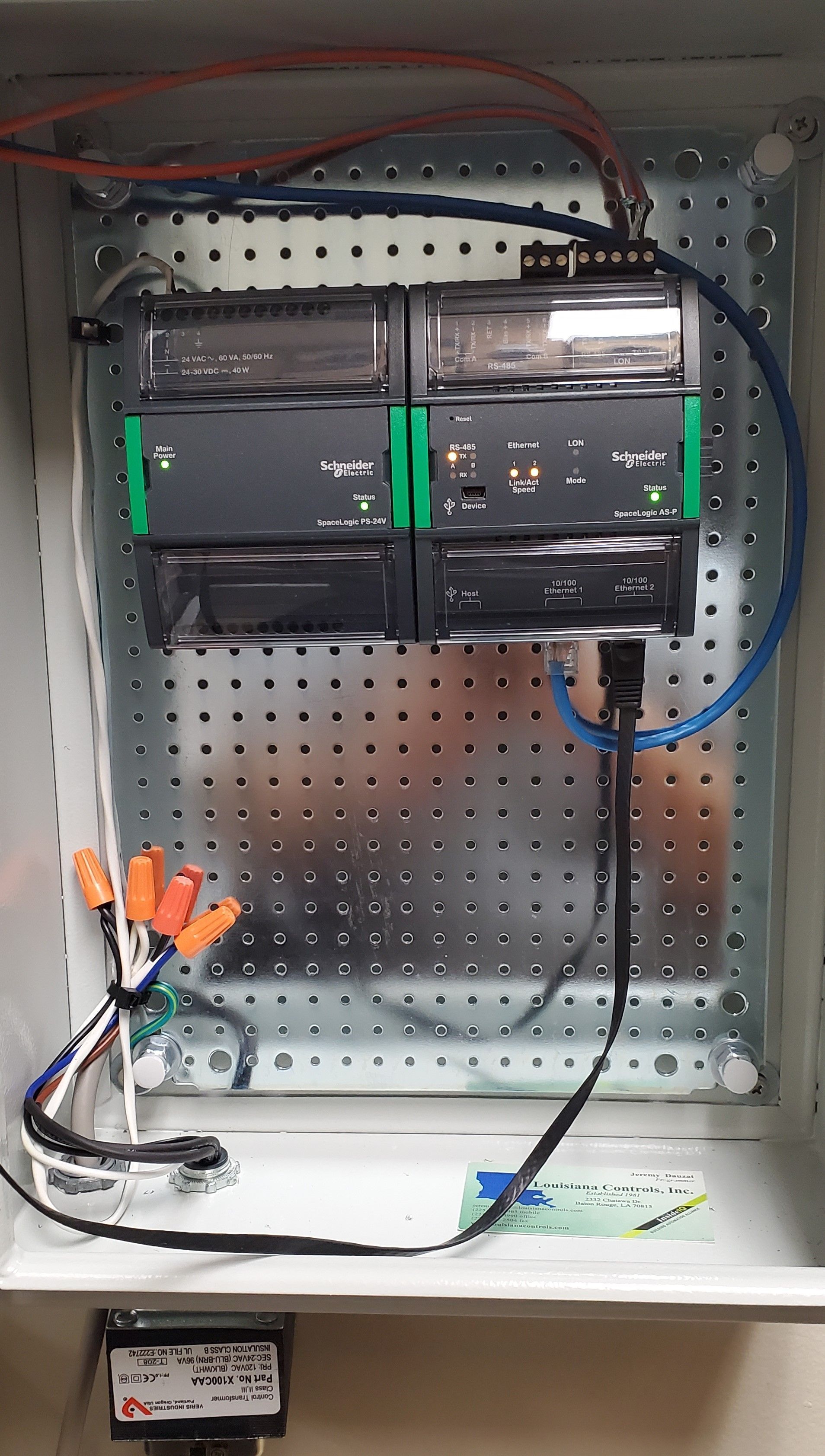 Open metal cabinet with black electrical/network equipment, cables, and a perforated back panel.
