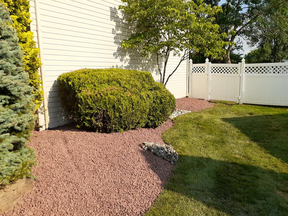 A white fence surrounds a lush green yard with a white house in the background.