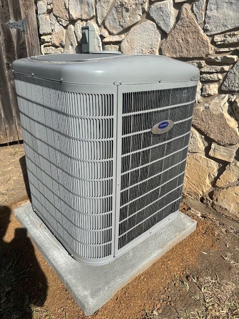 A carrier air conditioner is sitting on a concrete base in front of a stone wall.