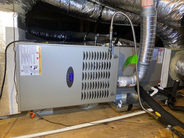 An air conditioner is sitting in a basement next to pipes.