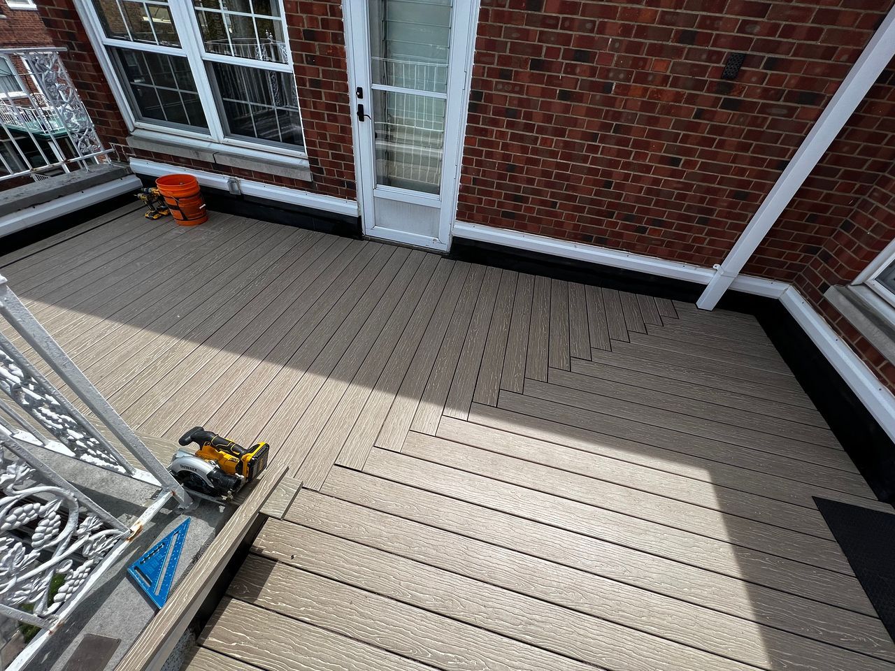 Composite deck with zig-zag design next to a brick building. Saw and bucket present.