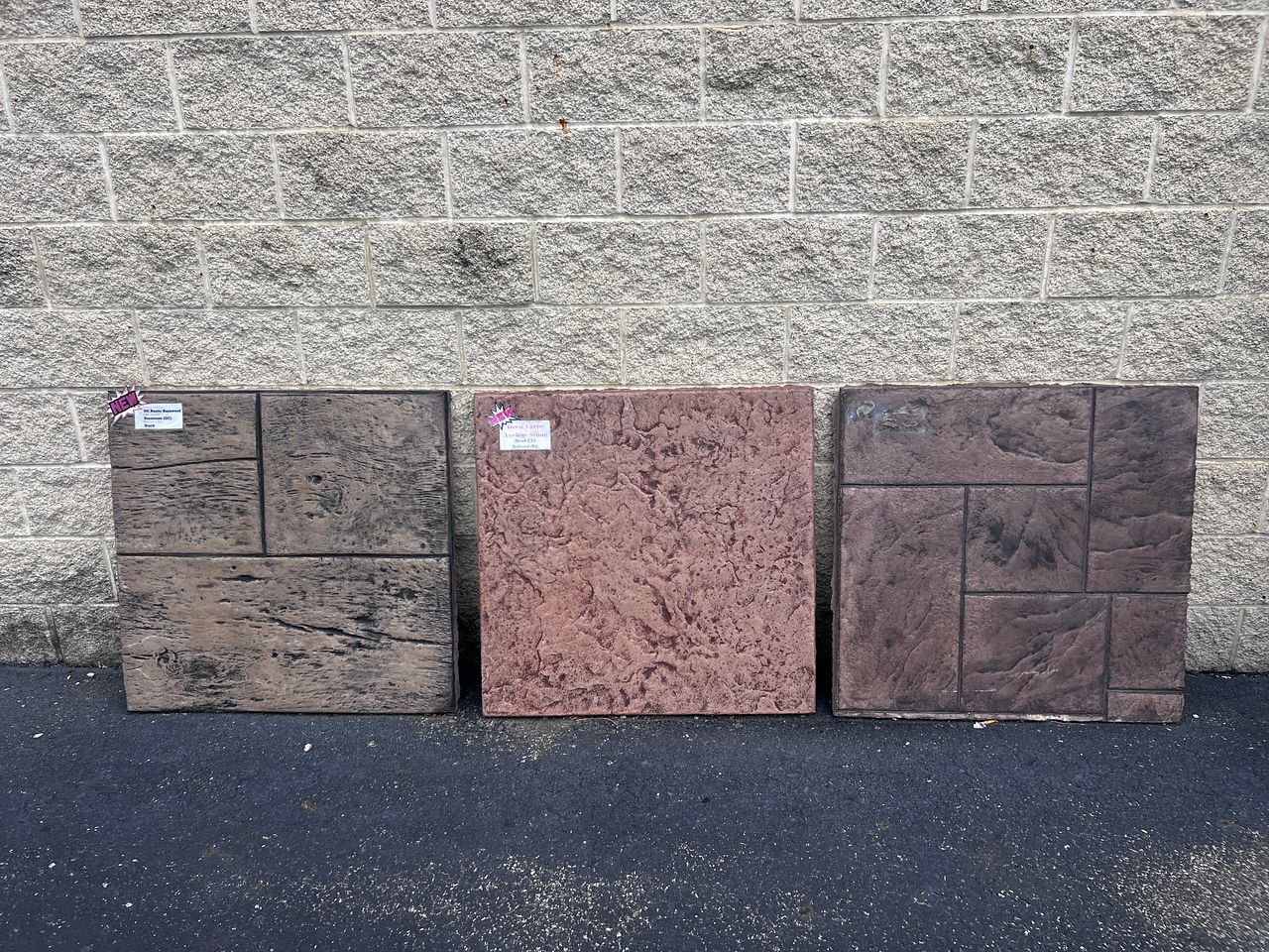 Three concrete pavers with different textures and colors against a brick wall.