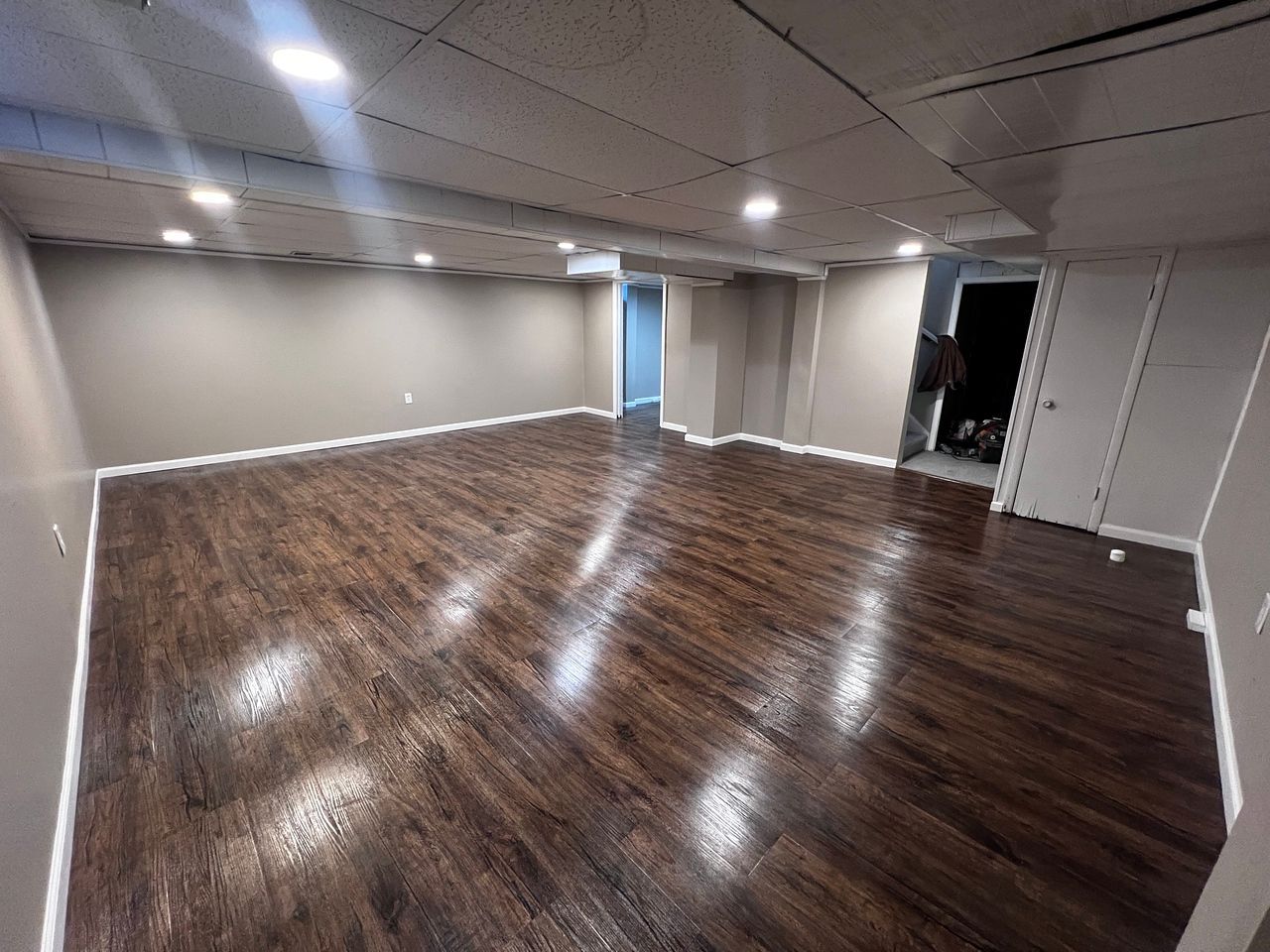 Empty room with dark wood-look floor, tan walls, recessed lighting, and a doorway.