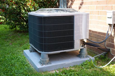 Outdoor air conditioning unit on a concrete pad beside a brick house and green lawn.