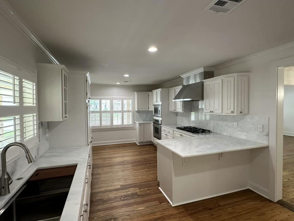 A kitchen with white cabinets , hardwood floors , a sink and a stove.