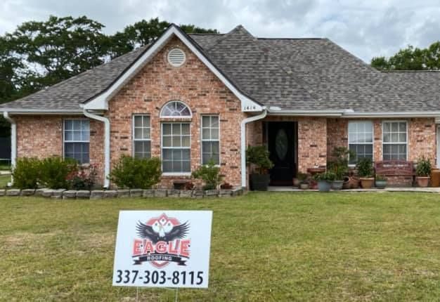 A brick house with a gray roof and a sign in front of it.
