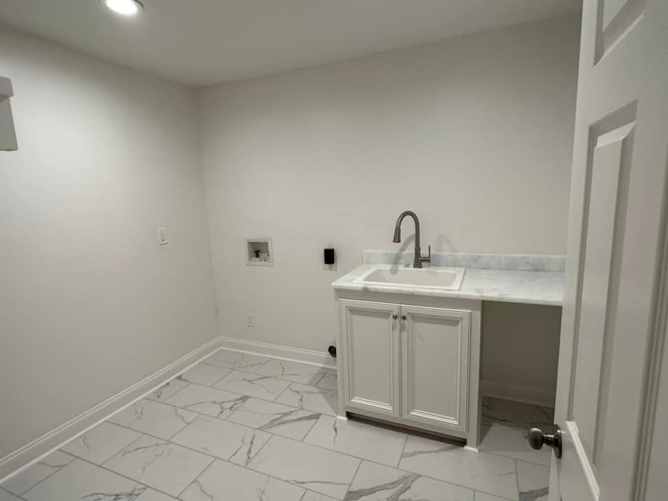 A laundry room with a sink and cabinets in a house.