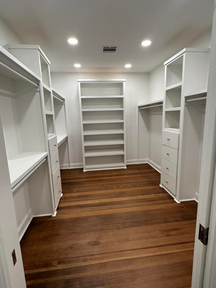 A walk in closet with hardwood floors and white shelves.