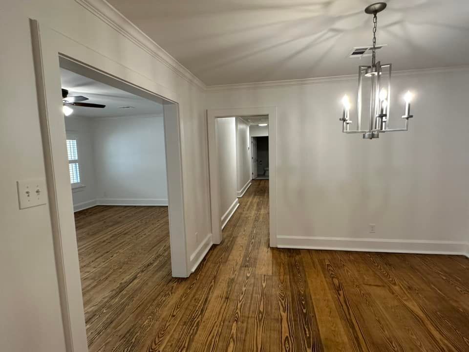 An empty dining room with hardwood floors and a chandelier hanging from the ceiling.
