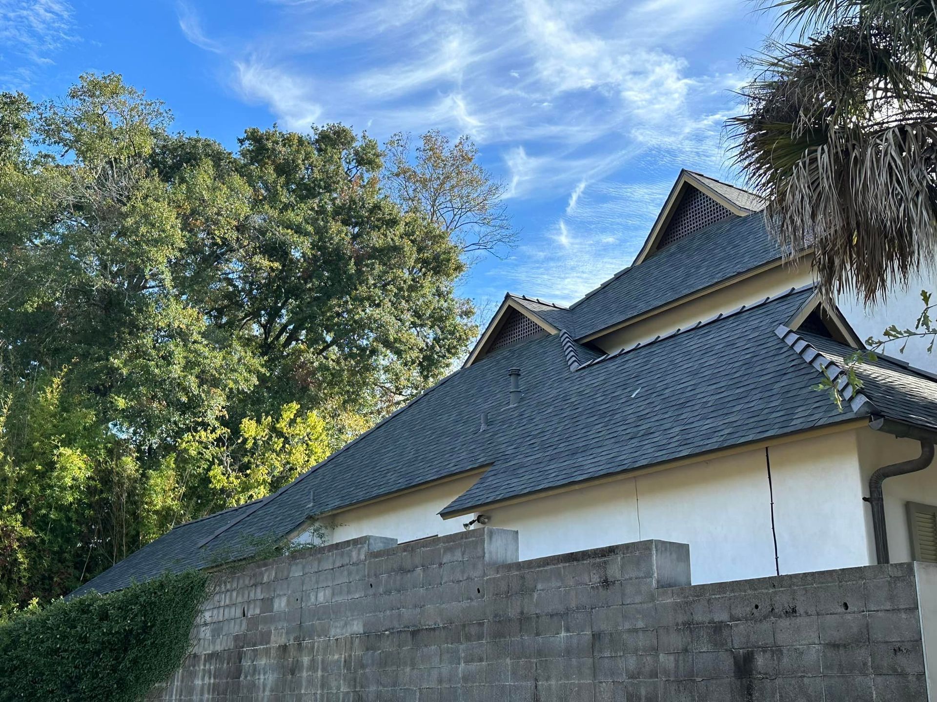 A white house with a gray roof and a brick wall in front of it.