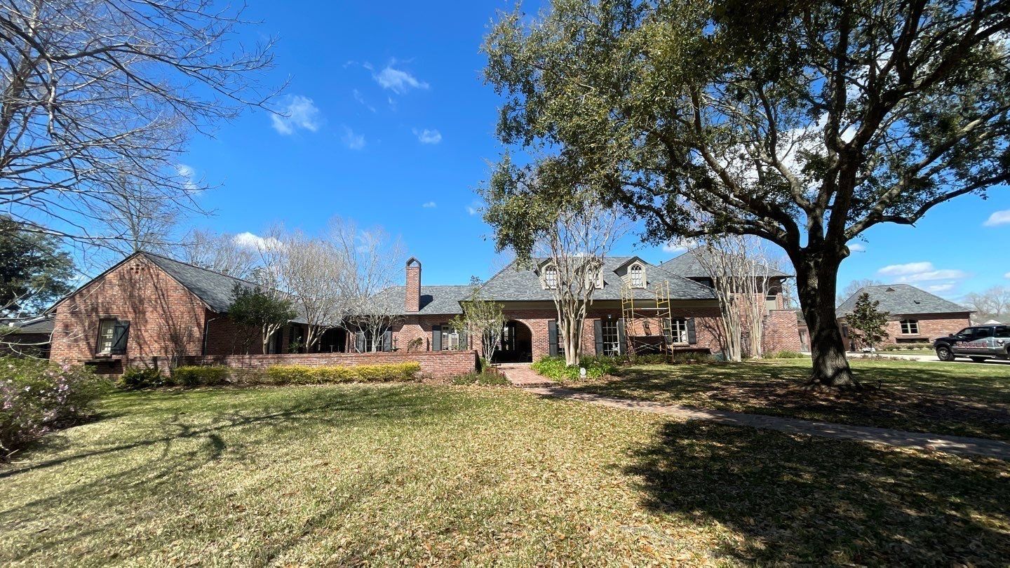 A large brick house with a large lawn and trees in front of it.