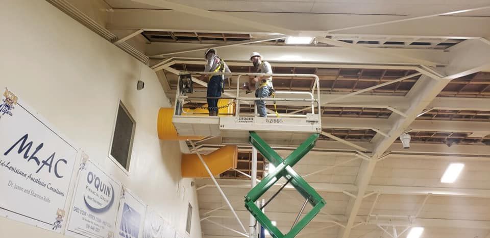 Two men are working on the ceiling of a building on a scissor lift.