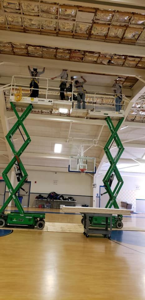 A group of people are working on a basketball court with scissor lifts.
