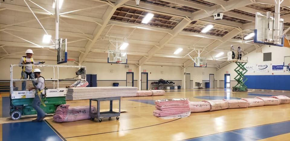 Two men are working on a basketball court in a gym.