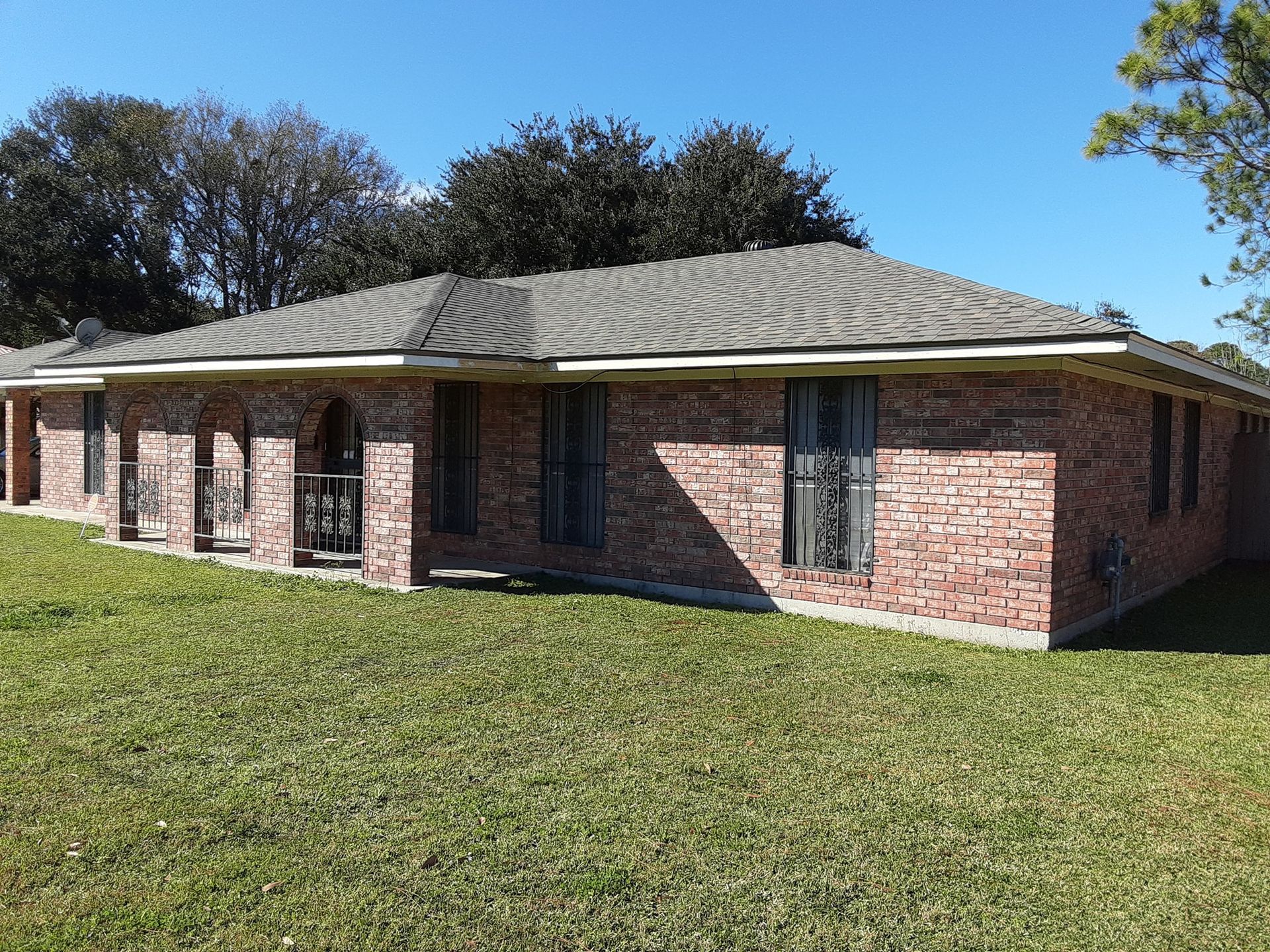 A brick house with a gray roof is sitting on top of a lush green field.