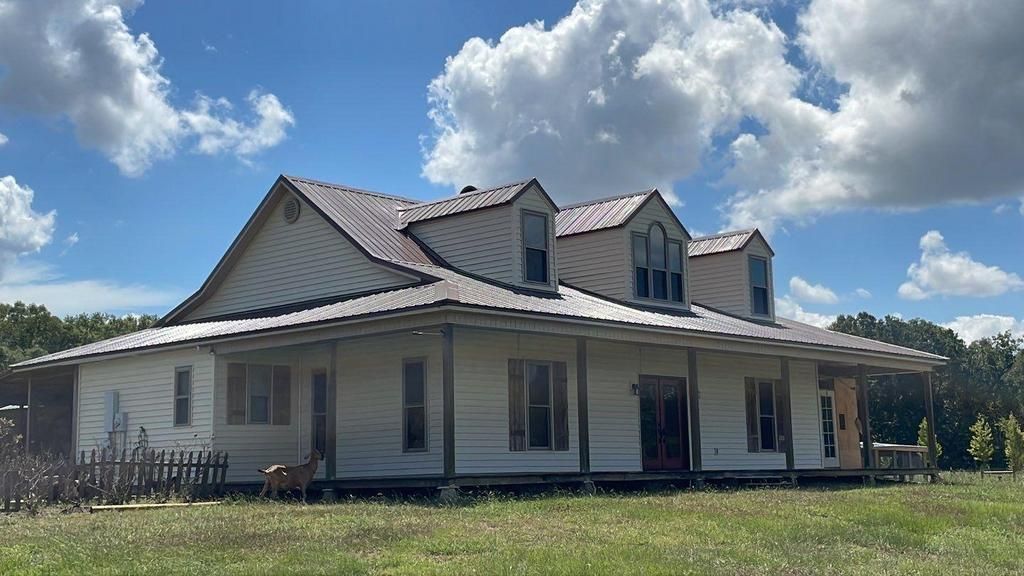 A large white house with a metal roof is sitting in the middle of a grassy field.