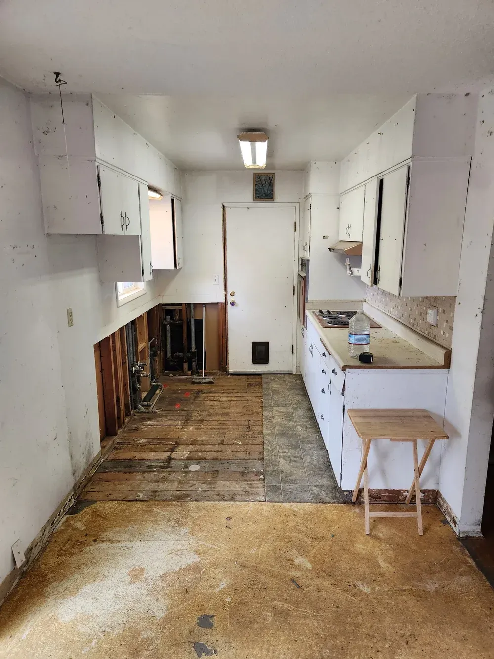 Kitchen in disrepair, cabinets, exposed wall studs, and damaged flooring, likely under renovation.