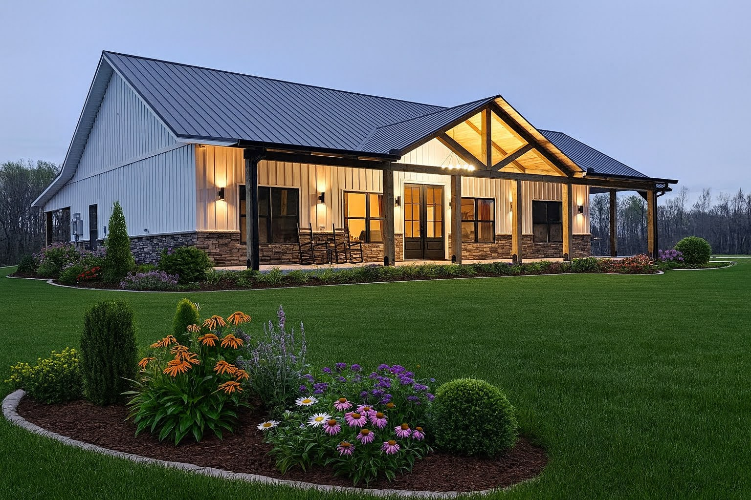 Modern white farmhouse at dusk with lit windows, metal roof, and landscaped flower beds on a green lawn
