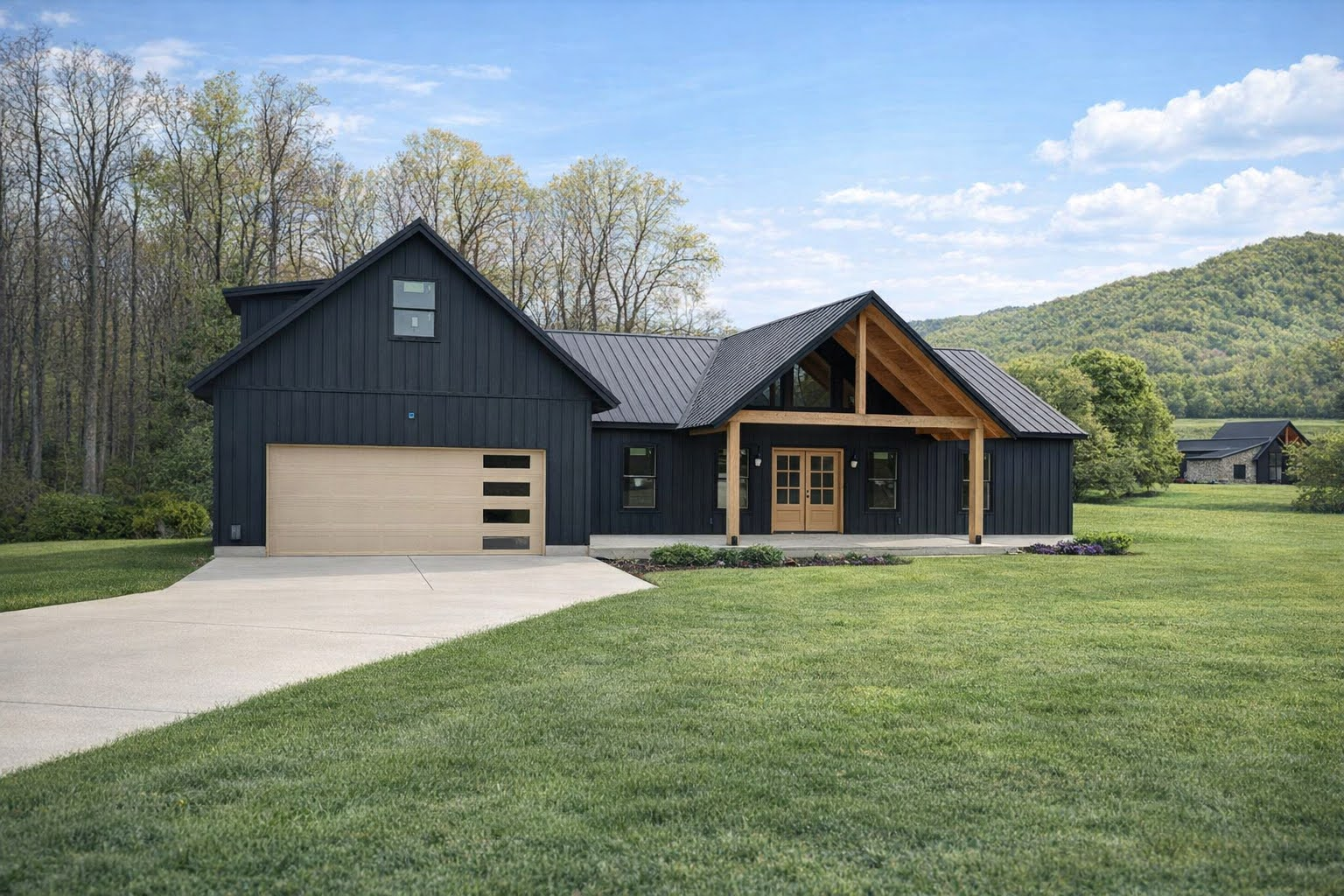 Modern black house with a gabled porch, attached garage, and large green lawn in a rural setting