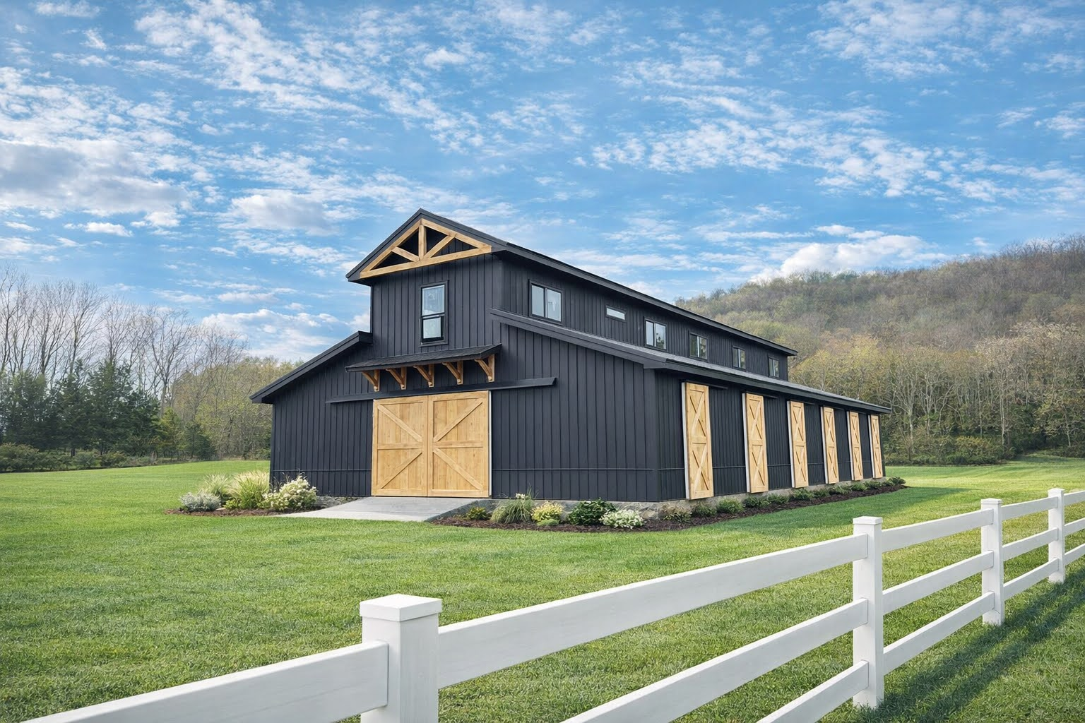 Black barn with tan doors in a grassy field beside a white fence under a blue sky