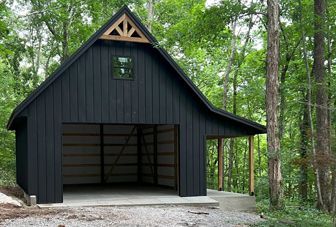 A black barn is sitting in the middle of a forest.