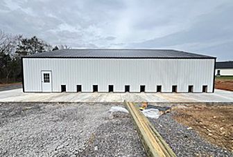 A large white building with a black roof is sitting on top of a gravel lot.