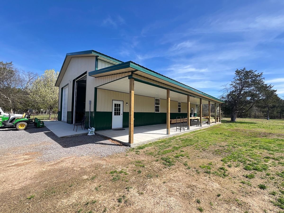 A green tractor is parked in front of a barn with a porch.