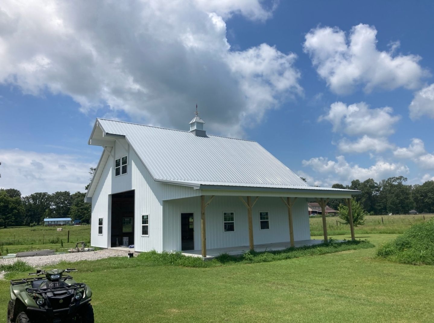 A white barn is sitting in the middle of a grassy field.