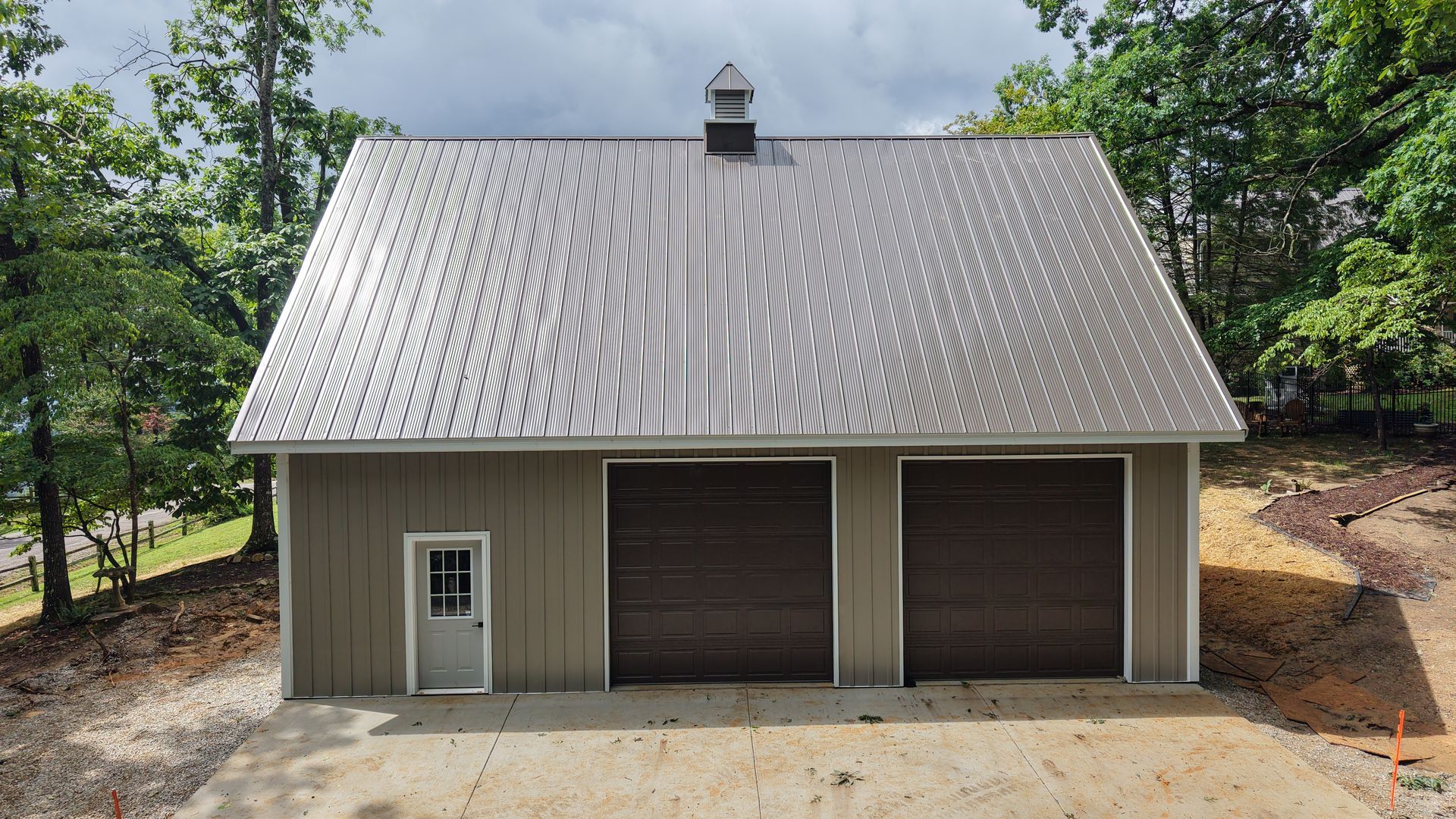 Two-car garage with brown doors, a gray roof, and a small side door; set in a wooded area.