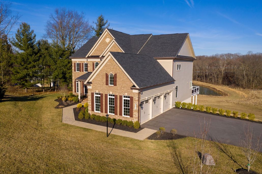 Brick suburban house with gray roof, attached garage, and large lawn on a sunny day
