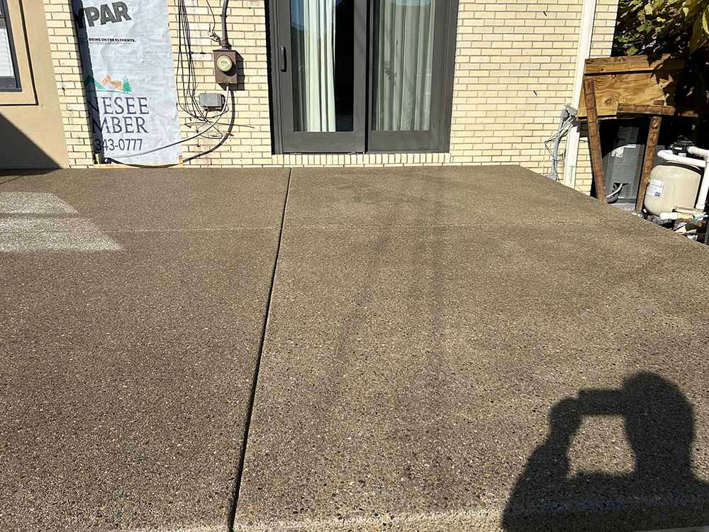 A concrete patio with a shadow of a person on it in front of a brick house.